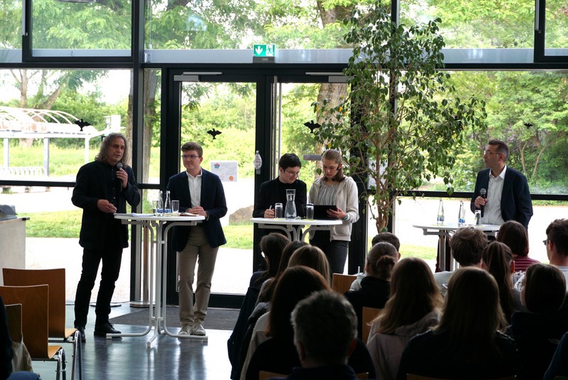 5: Großaufnahme der Podiumsdiskussion mit drei Bewerbern und Moderatorinnen